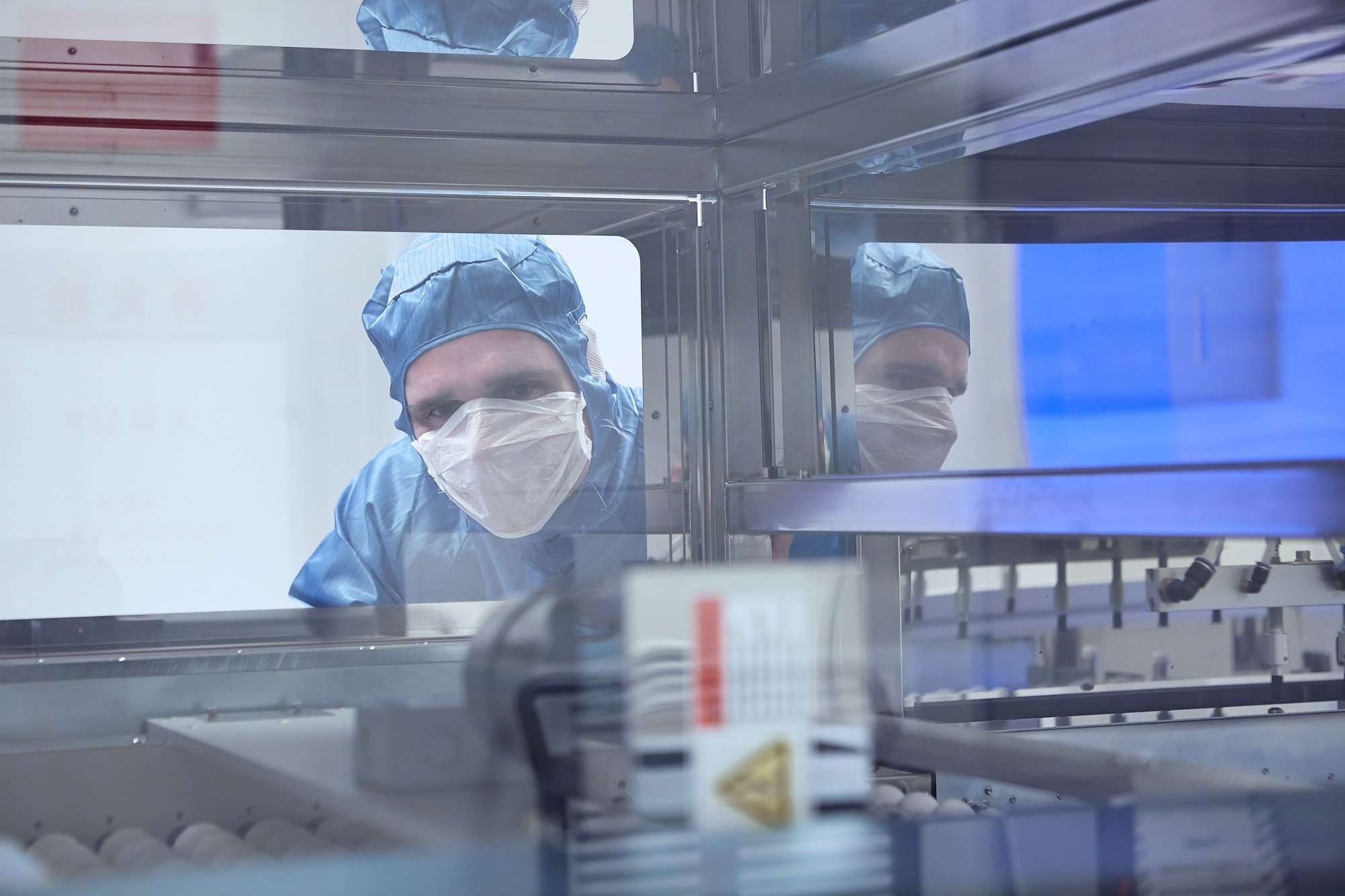 Male worker looking through machine window in flexible electronics factory clean room